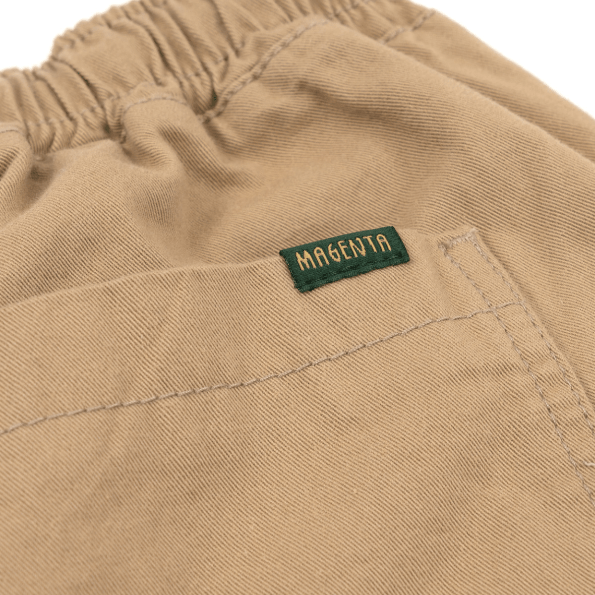 Beige Magenta Skateboards Slack Pants, casual trousers with relaxed fit and skateboard-inspired style, shown on a plain background.