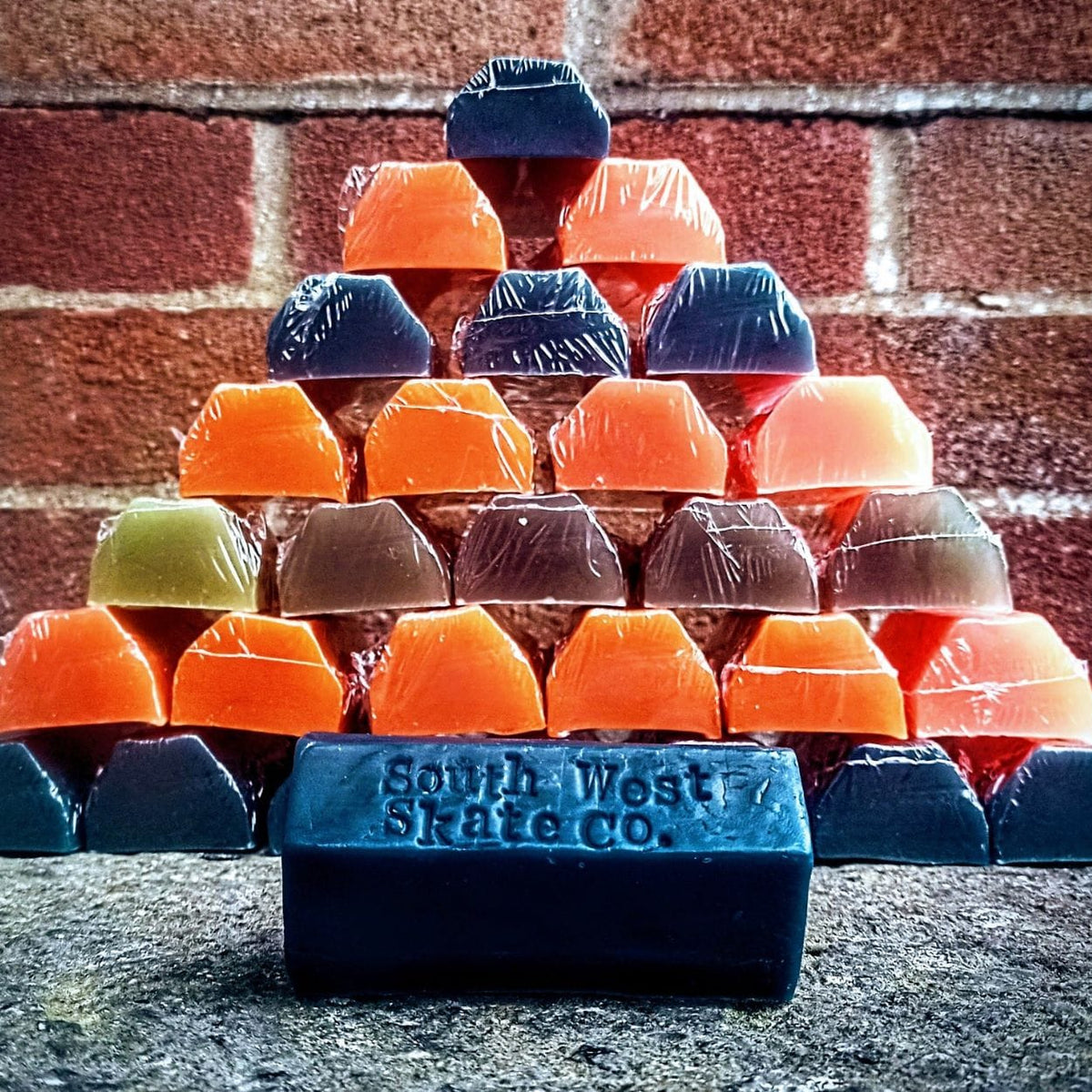 Orange skateboard wax by South West Skate Co, showing a small container of wax used for grip and maintenance on skateboards.