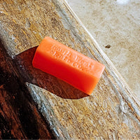 Orange skateboard wax by South West Skate Co, shown in a container with the label visible for smooth grip and skating performance.