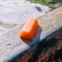 Orange skateboard wax from South West Skate Co, showing a container of wax on a wooden surface.